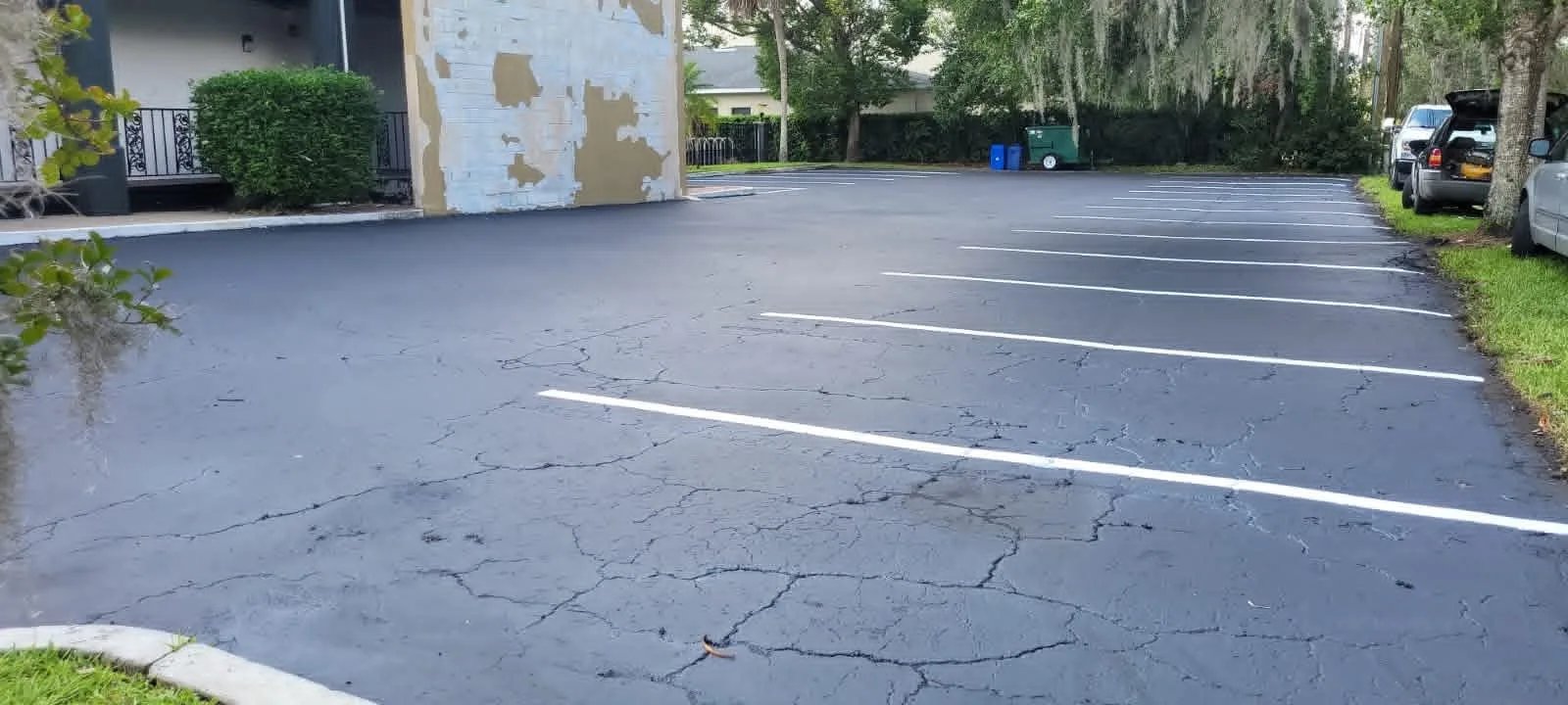 Sealcoated parking lot with fresh striping and visible asphalt cracks