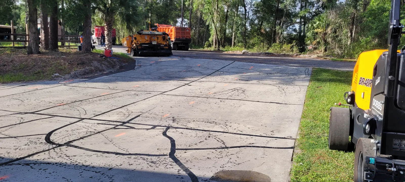 Cracked asphalt driveway with extensive damage and paving equipment in the background