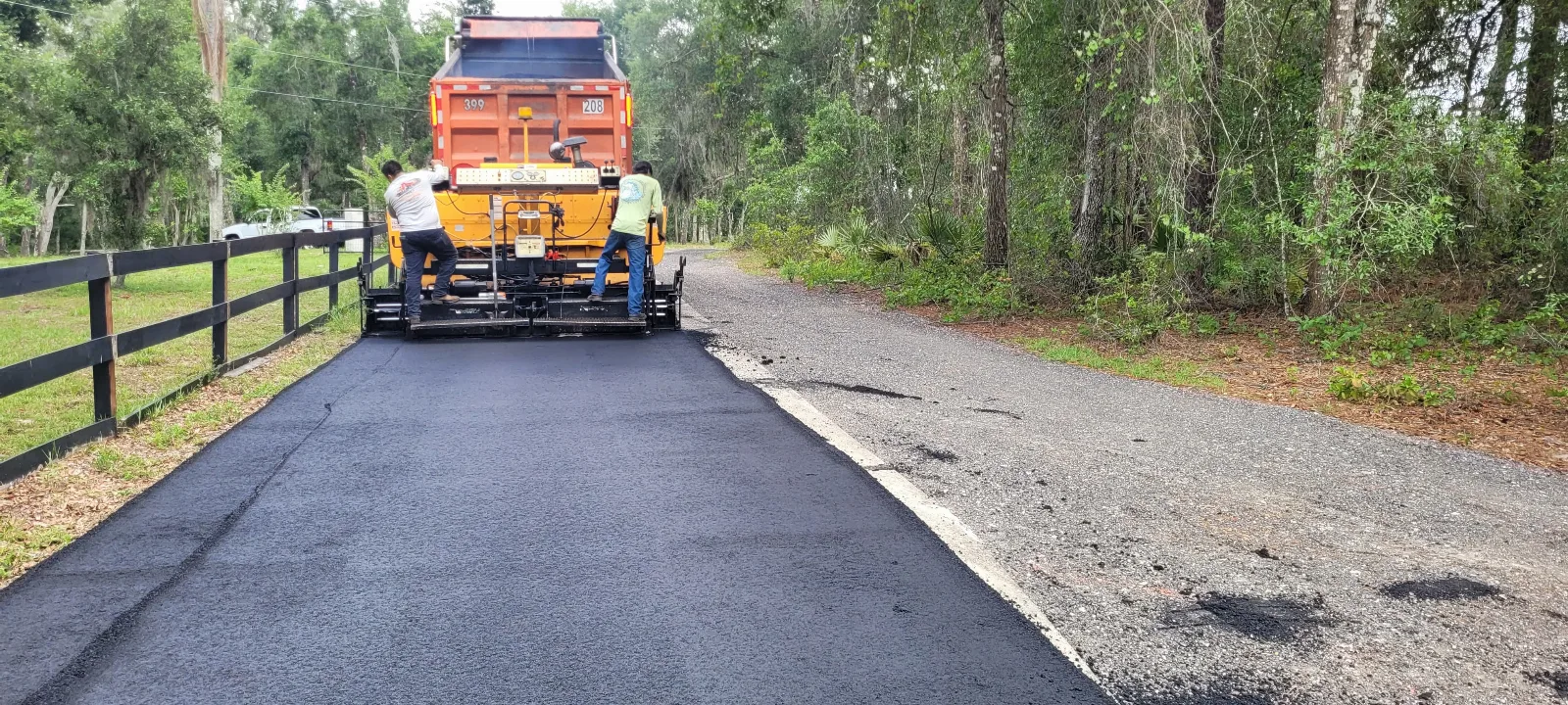 Workers paving a residential driveway with fresh asphalt using professional equipment