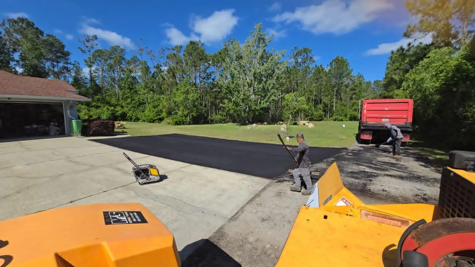 Crew paving a residential community driveway with fresh asphalt and heavy equipment