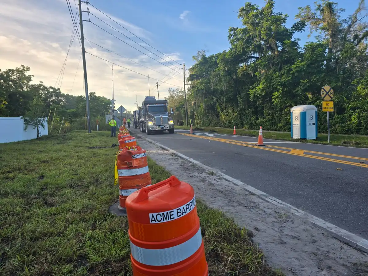 Orange drums along the shoulder of an old two lane road in Daytona Beach, Florida, with a flagger and a dump truck at the far end
