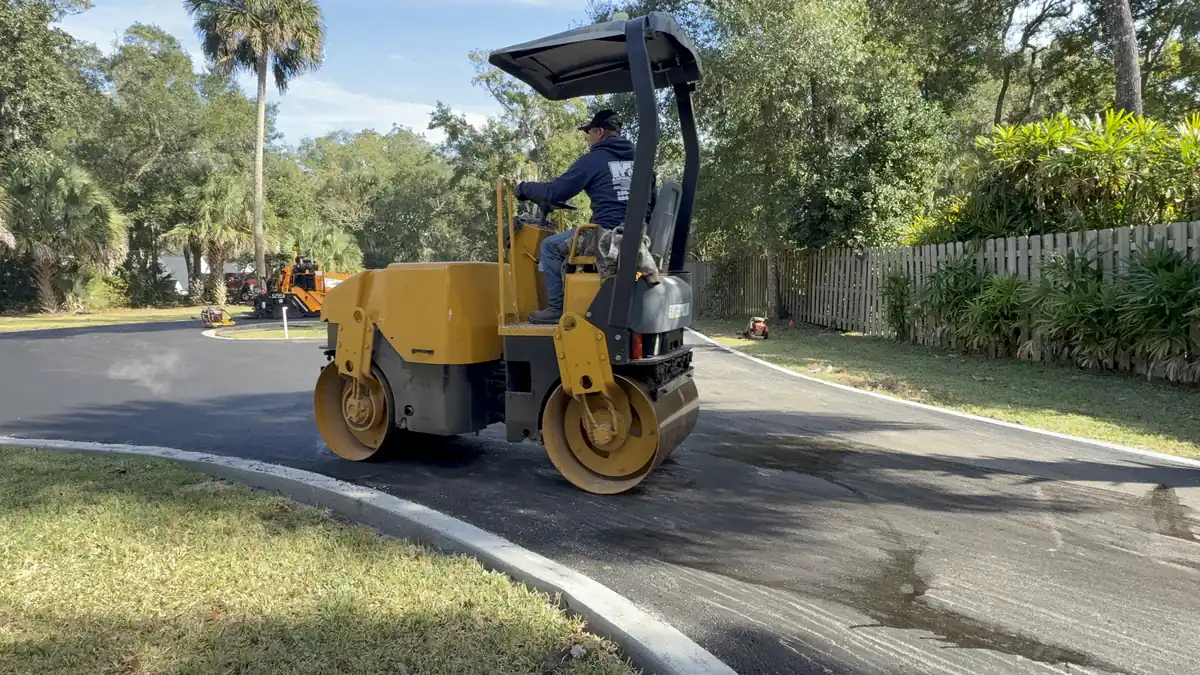 Operator running a tandem drum roller along the curb edge of a newly paved DeLand cul-de-sac