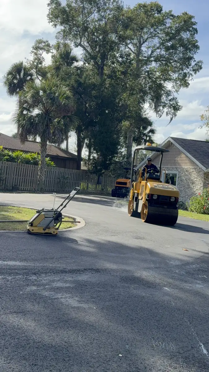 Roller passing a house on the DeLand cul-de-sac while a plate compactor sits at the island curb