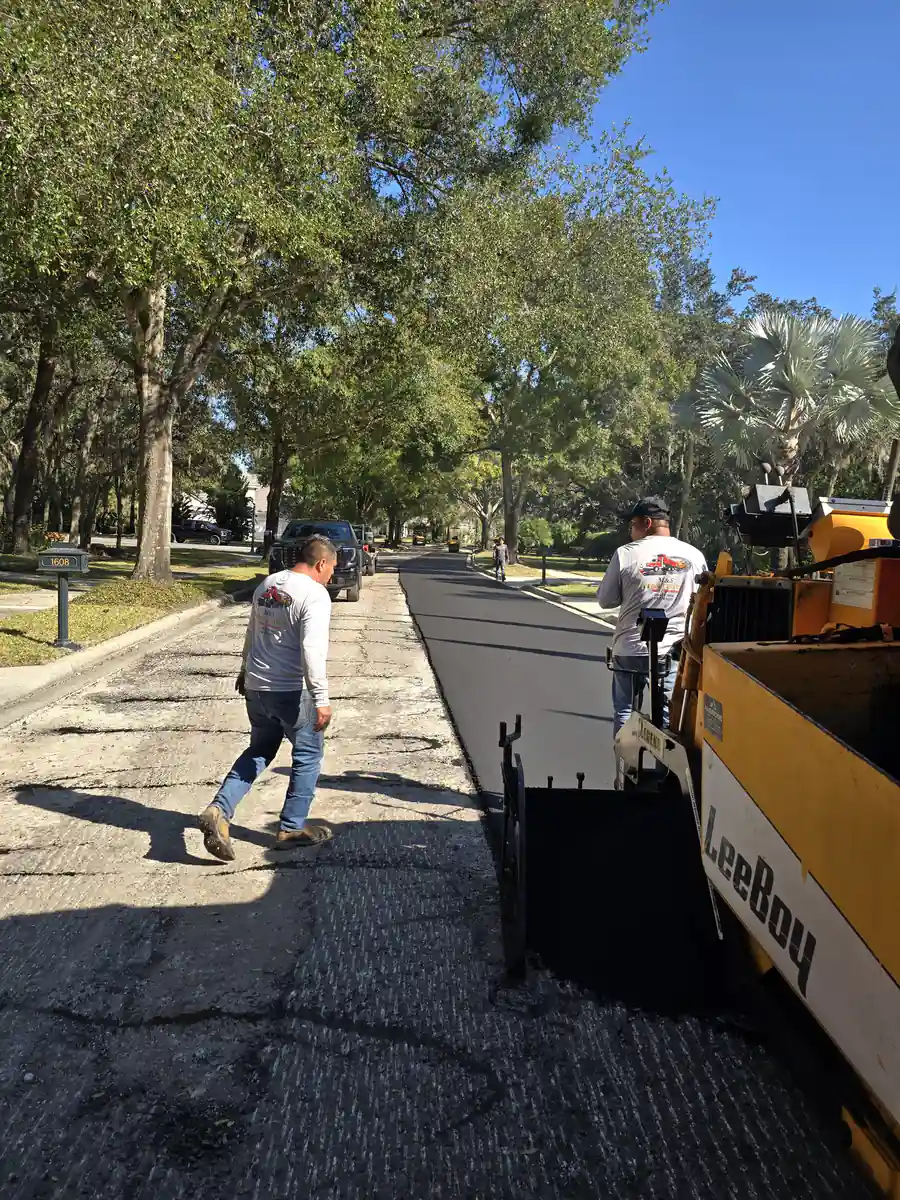 LeeBoy paver laying a new asphalt mat on a Sanford residential street while two crew members work the edge and joint