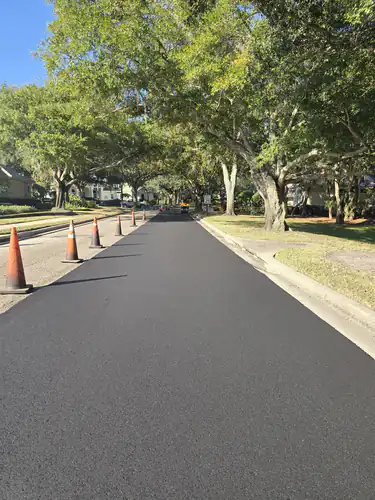 Finished black asphalt on a tree-lined residential street in Sanford, Florida, with traffic cones still lining the left edge