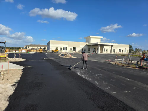 During paving: crew member leveling fresh asphalt with a long-handled lute in front of a new commercial building in Sanford, Florida