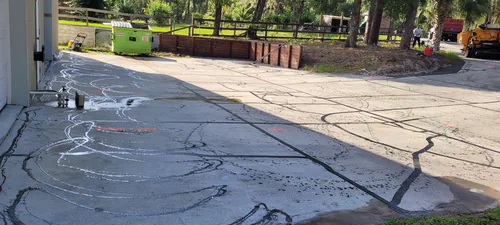 Before: close view of a pale cracked driveway in Ormond Beach with wavy black crack sealer lines and swirls from an old sealcoat job