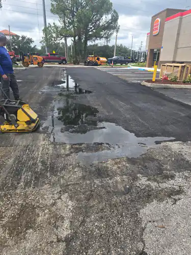 Fresh asphalt at an Orlando shopping complex with a yellow bollard and new curbed planter in front of the storefront