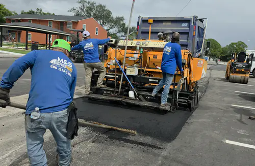 Dump truck feeding hot asphalt into the paver as M&S Asphalt Paving crew members start a pass on an apartment complex lot in DeBary, Florida