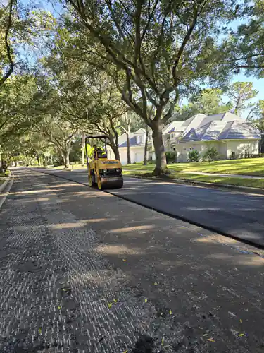 Roller compacting the freshly paved half of a tree-lined DeLand street beside the milled half still open to traffic