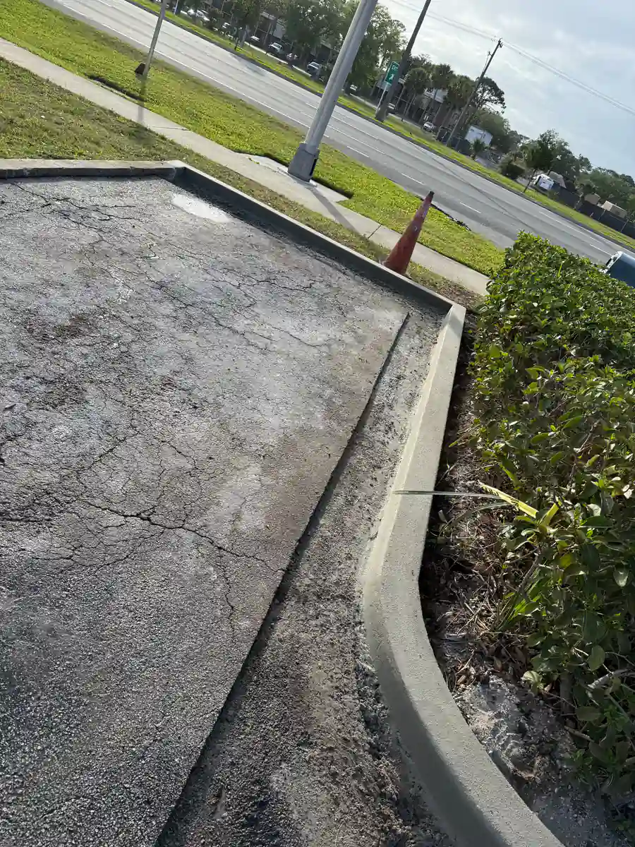 New concrete curb running along the end of a parking bay beside heavily cracked older asphalt in a DeLand, Florida lot