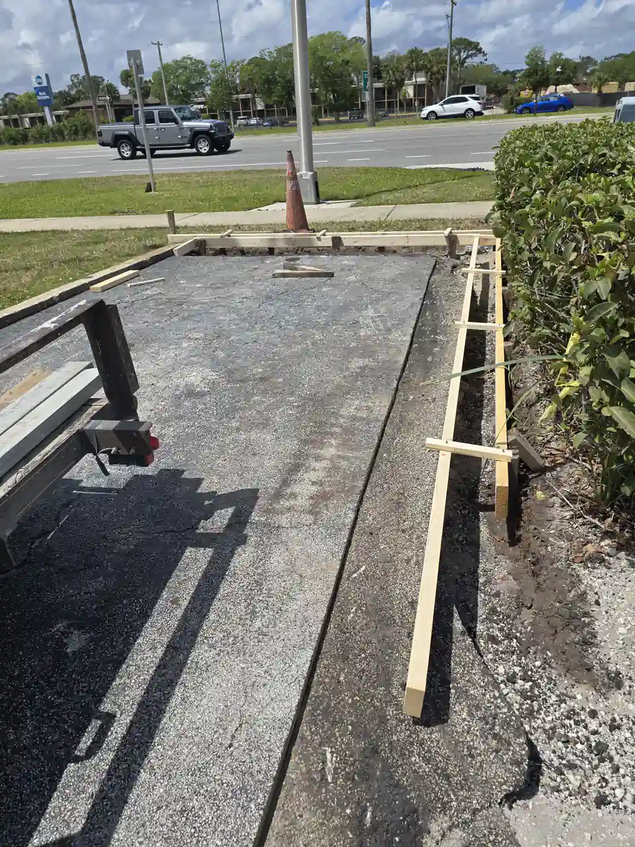 Timber forms and stakes set along a trench cut into an old asphalt parking lot in DeLand, Florida, ready for a concrete curb pour