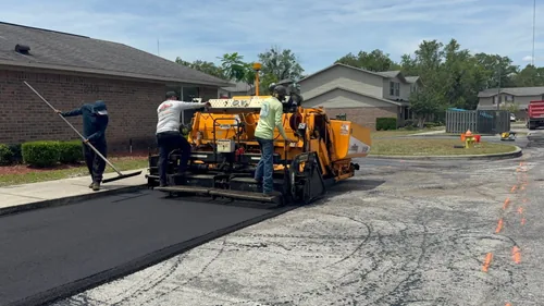 Two M&S Asphalt Paving crew members operating an asphalt paver machine on a residential driveway