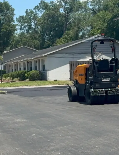 Paver and roller finishing a parking lot beside a new concrete curb