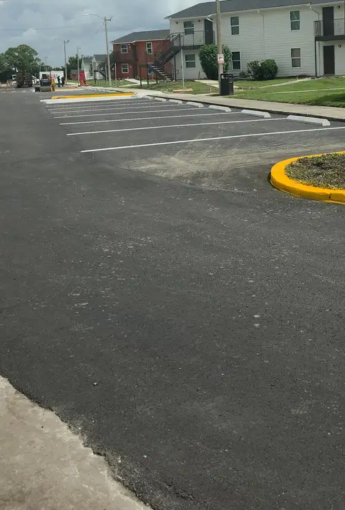 Row of new concrete curb stops along a freshly striped apartment parking lot with a yellow painted curb island