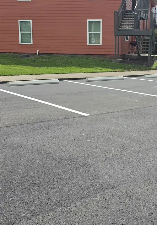 Concrete curb stops set in front of freshly striped parking spaces beside a sidewalk and apartment building