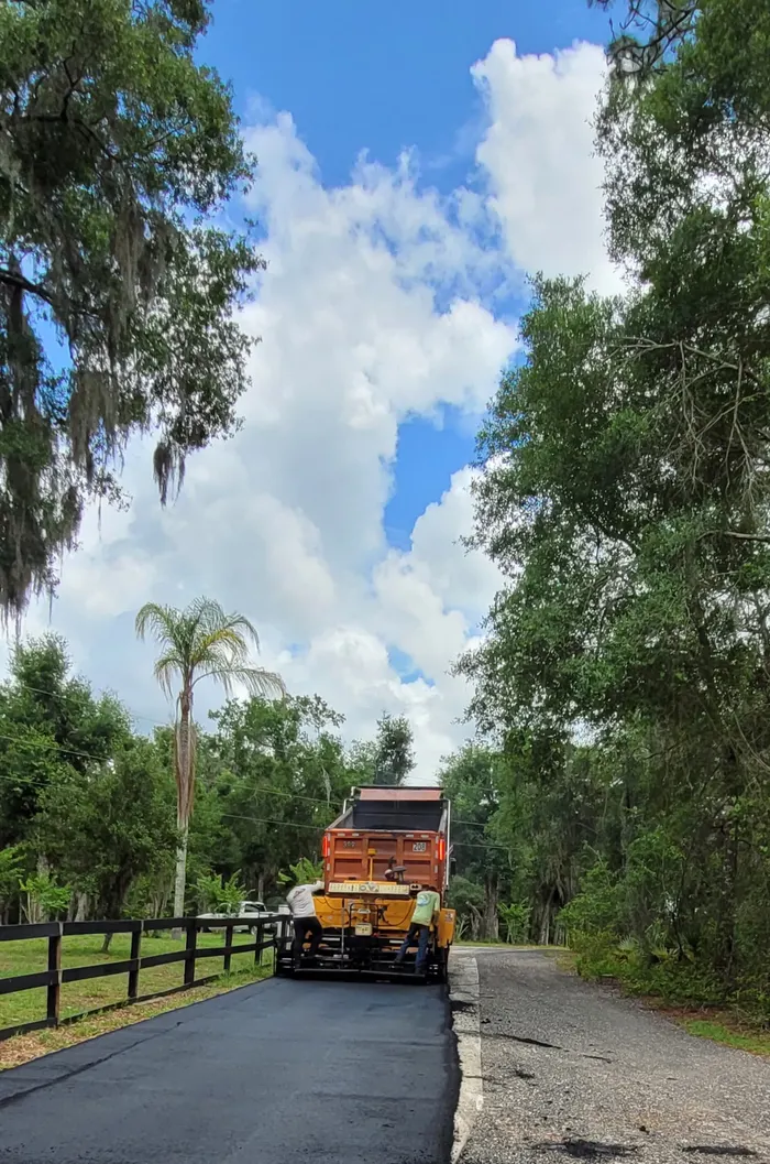 M&S Asphalt Paving dump truck feeding a paver on a tree lined Central Florida road