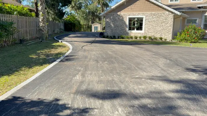 Freshly paved residential driveway curving past a stone-front home