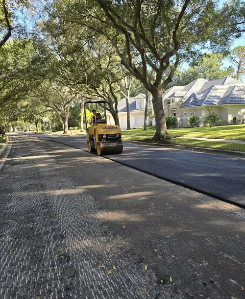 Roller compacting fresh asphalt on a tree-lined residential street in DeLand, Florida