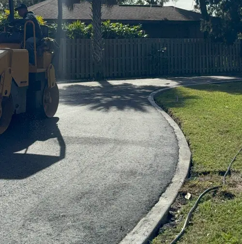 Roller finishing a curved residential driveway behind a wooden fence in DeLand, Florida