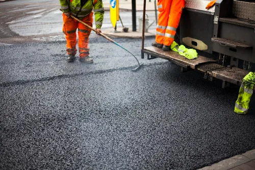 Crew in high visibility gear spraying sealcoat across an asphalt surface